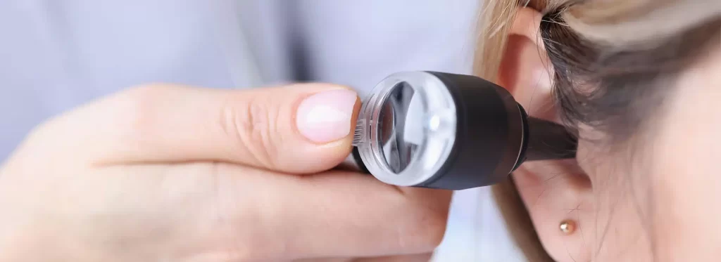 Chiropractor using otoscope to examine patient's ear, important for diagnosing conditions related to balance and posture affecting spinal alignment.