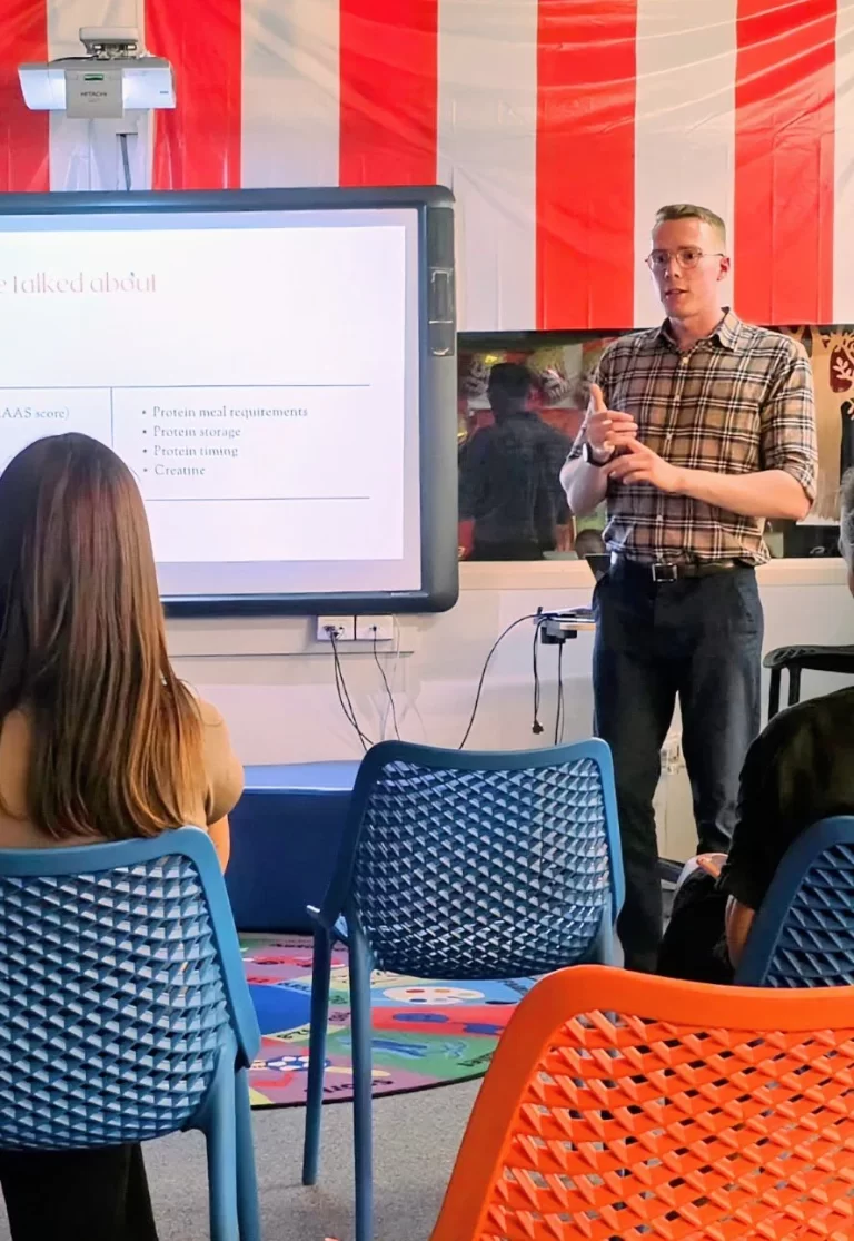 Chiropractor or health professional giving a presentation on protein requirements and timing to an audience, potentially related to nutrition and recovery for chiropractic patients.