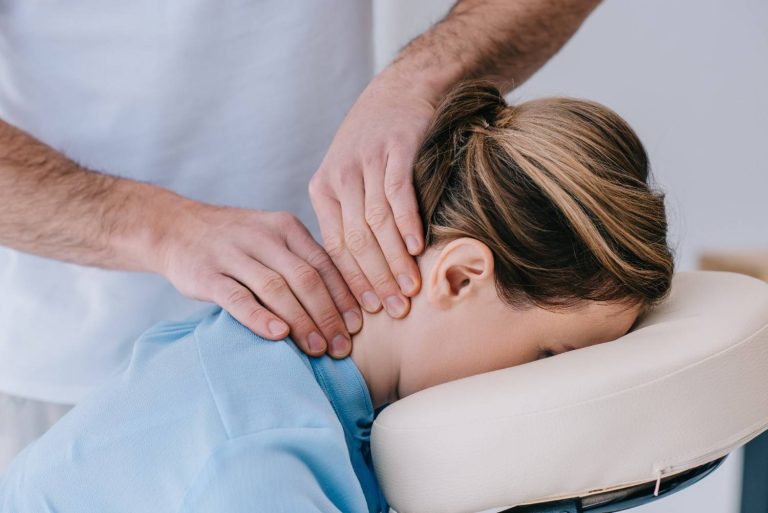 Chiropractor performing neck adjustment on female patient lying face down on chiropractic table.