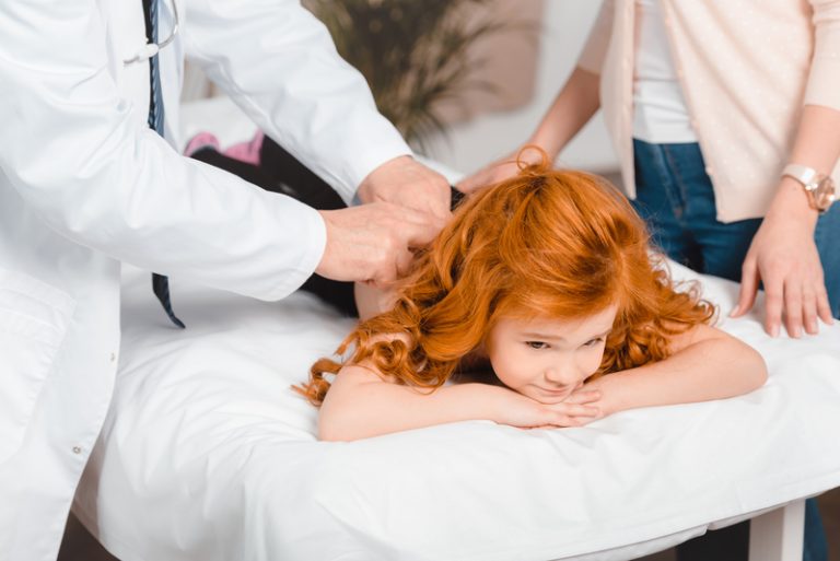 Young girl receiving chiropractic treatment from a chiropractor, with her mother present, focusing on pediatric chiropractic care.