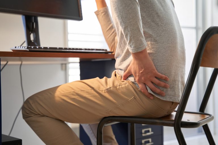 Man experiencing lower back pain while sitting at a desk, potentially needing chiropractic care for spinal alignment and pain relief.