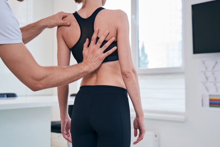 Chiropractor examining a female patient's back for spinal alignment and providing chiropractic treatment.