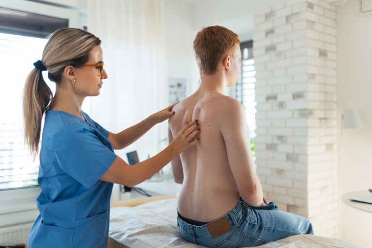 Chiropractor examining a young man's back for spinal alignment, providing chiropractic treatment.