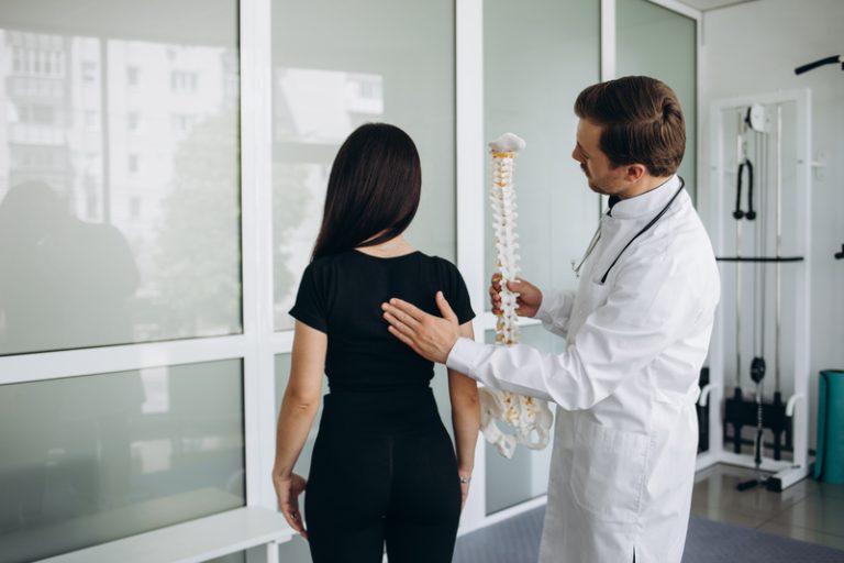 Chiropractor examining patient's spine, using spinal model to explain treatment.