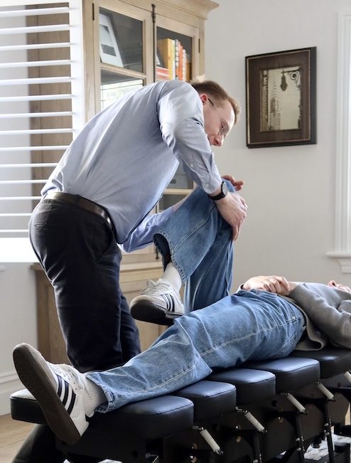 Chiropractor performing leg adjustment on patient lying on chiropractic table.